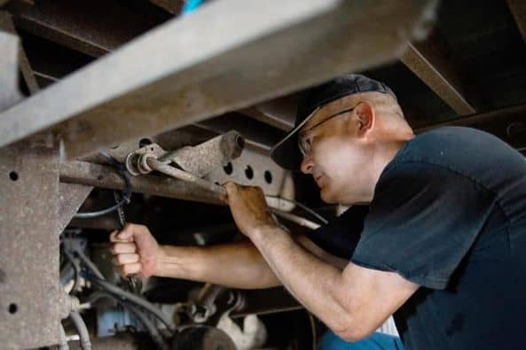 Technician performing trailer maintenance under frame to inspect components and prevent breakdowns